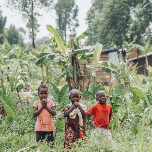 Tre barn som står framför en by i djungeln